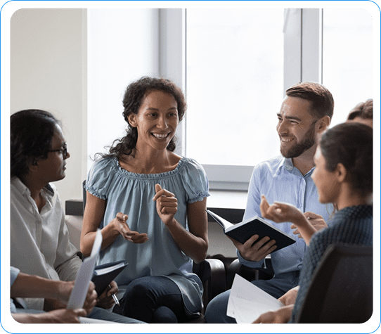 Group of people in a meeting discussing sales strategies, holding notebooks in a modern office.