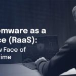 Image of hooded figure using laptop with shield, representing RaaS as the new face of cybercrime.